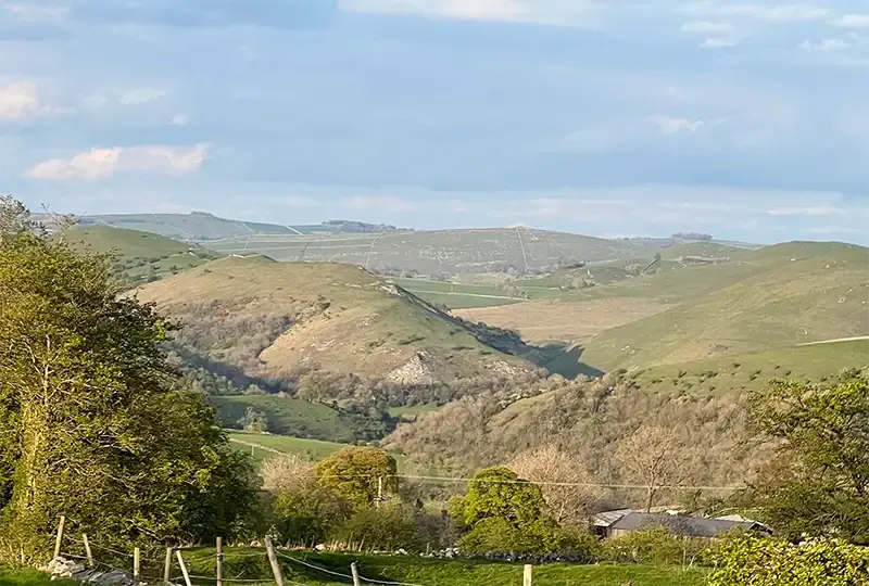 Rolling green hills with woodland valleys and scattered farm buildings in a rural landscape.