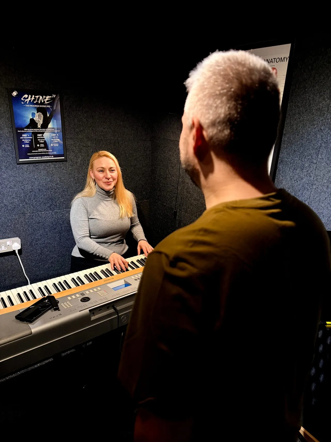 Woman and man having a piano lesson in a music studio with posters on the wall.