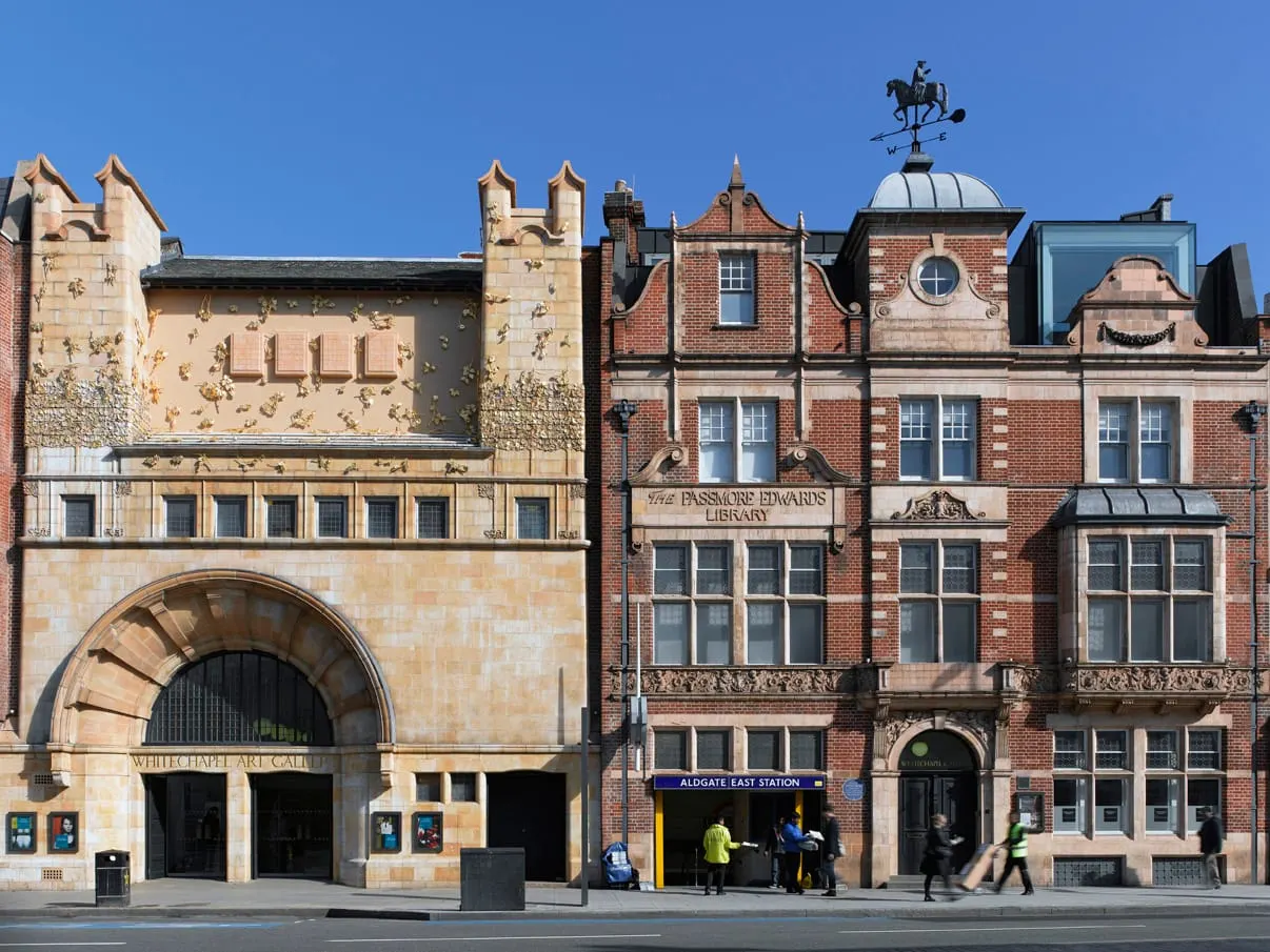 Historic stone and brick buildings housing the gallery and library, with pedestrians on the street below under clear blue sky.
