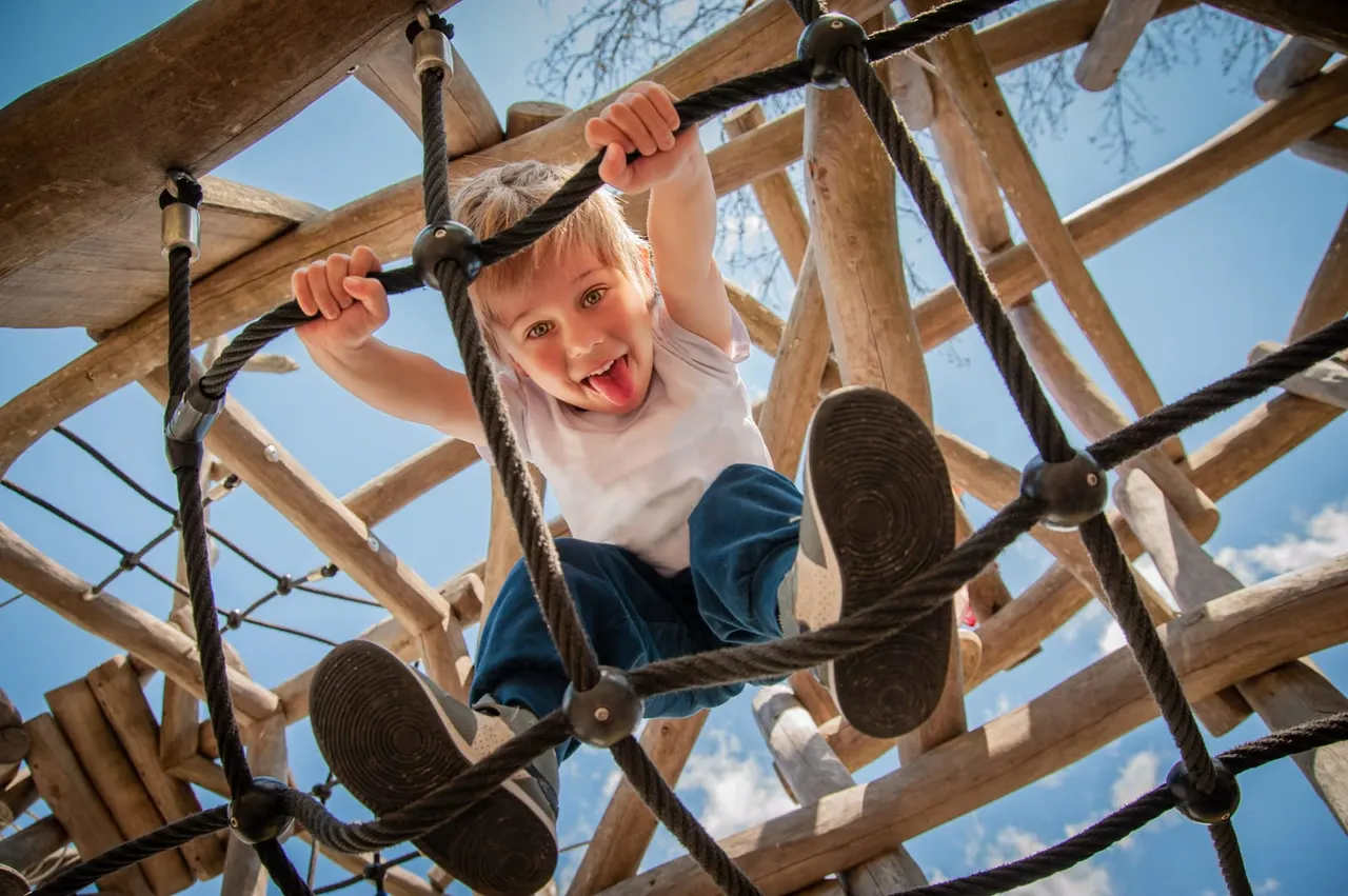 Young child climbing wooden rope course structure outdoors on a sunny day.
