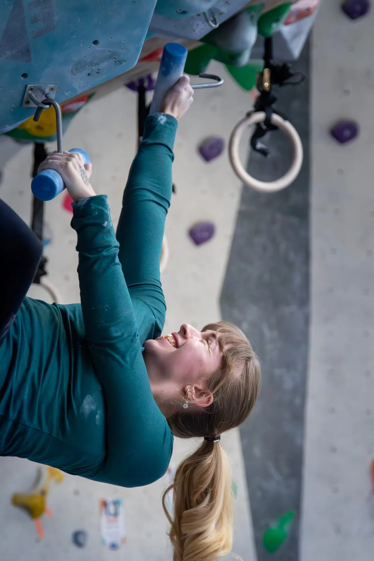 Child indoor rock climbing on a bouldering wall whilst gripping coloured handholds and rings.