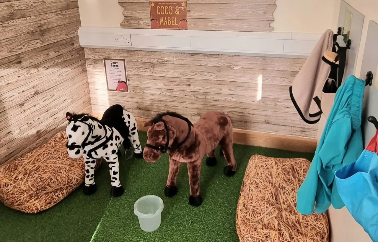 Toy farm animals on artificial grass in an indoor play area with wooden wall panelling.