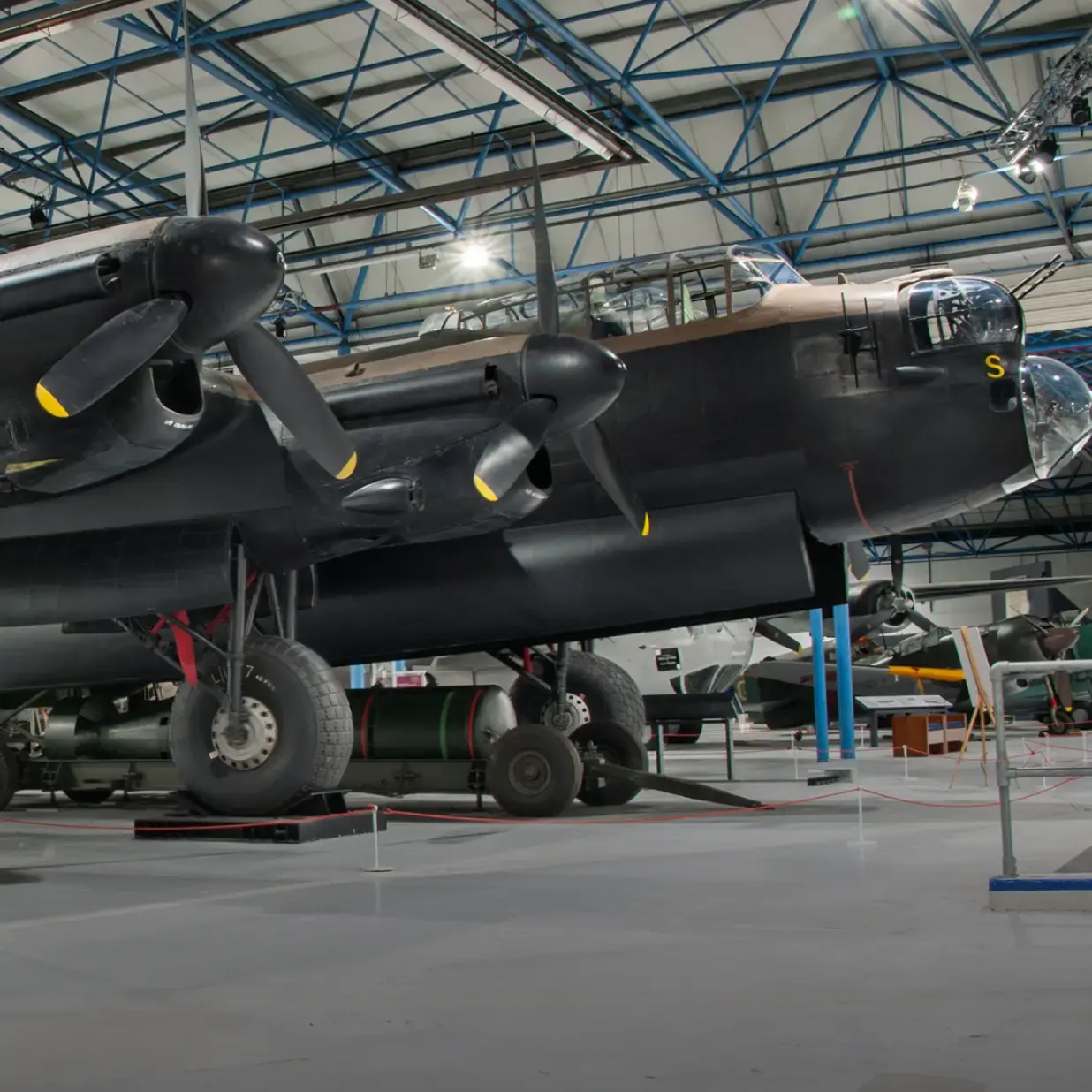 A black four-engine military aircraft on display inside a large hangar with blue steel framework and industrial lighting.
