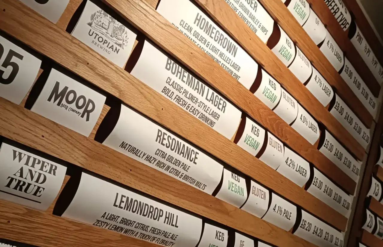 Wooden shelves displaying beer kegs with white labels showing names and descriptions of various craft beers.