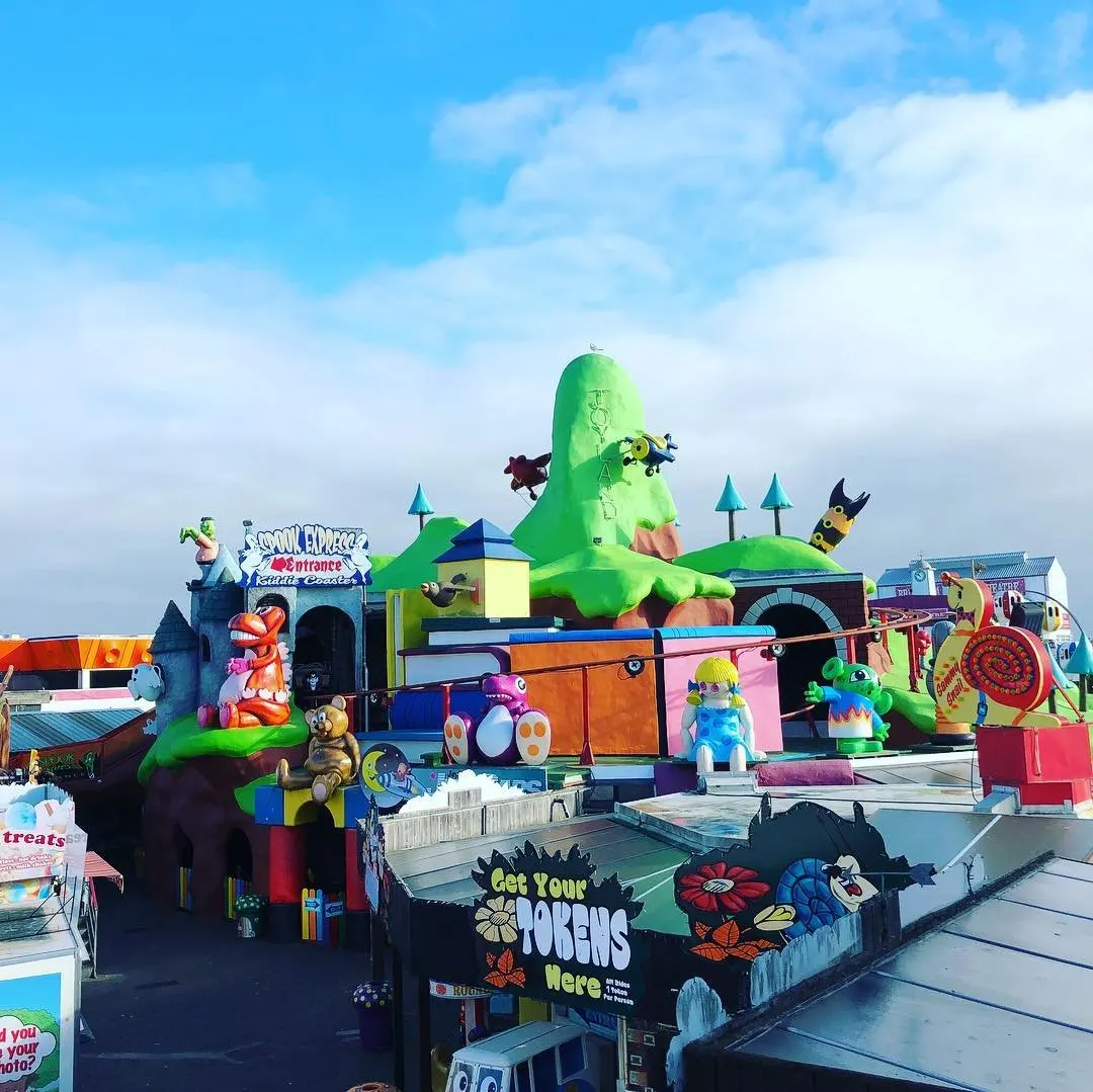 Colourful fairground ride with cartoon characters and bright green inflatable structures against a blue sky.