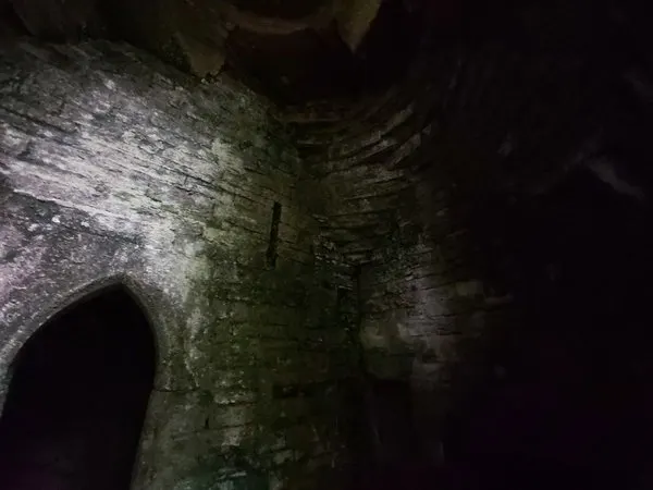 Stone archway and moss-covered walls inside an underground grotto, lit by artificial lighting.