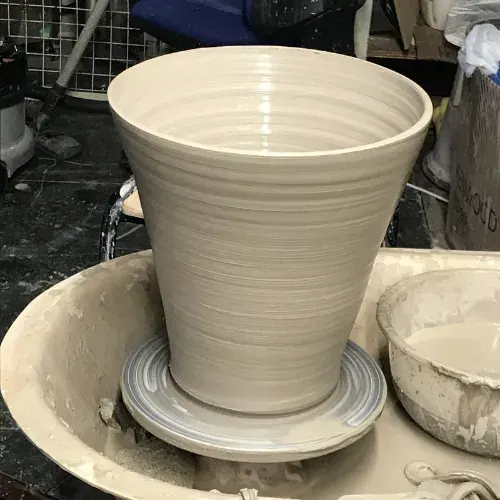 A freshly thrown ceramic vessel on a pottery wheel with a saucer base.