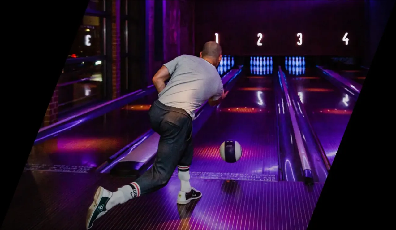 Man bowling down a lane in neon-lit alley with ball approaching pins.