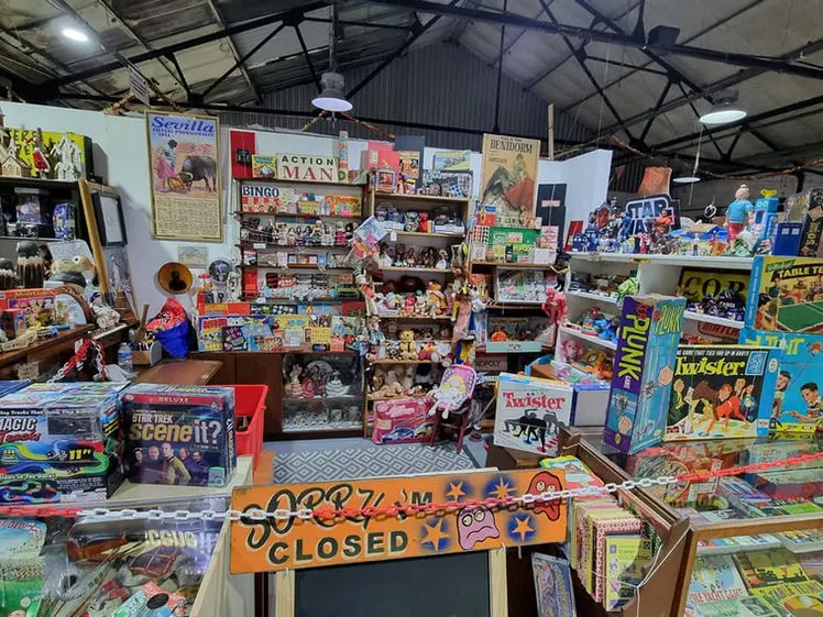 A vintage toy and memorabilia stall inside a flea market, displaying collectible board games, action figures, and retro merchandise on shelves and tables.