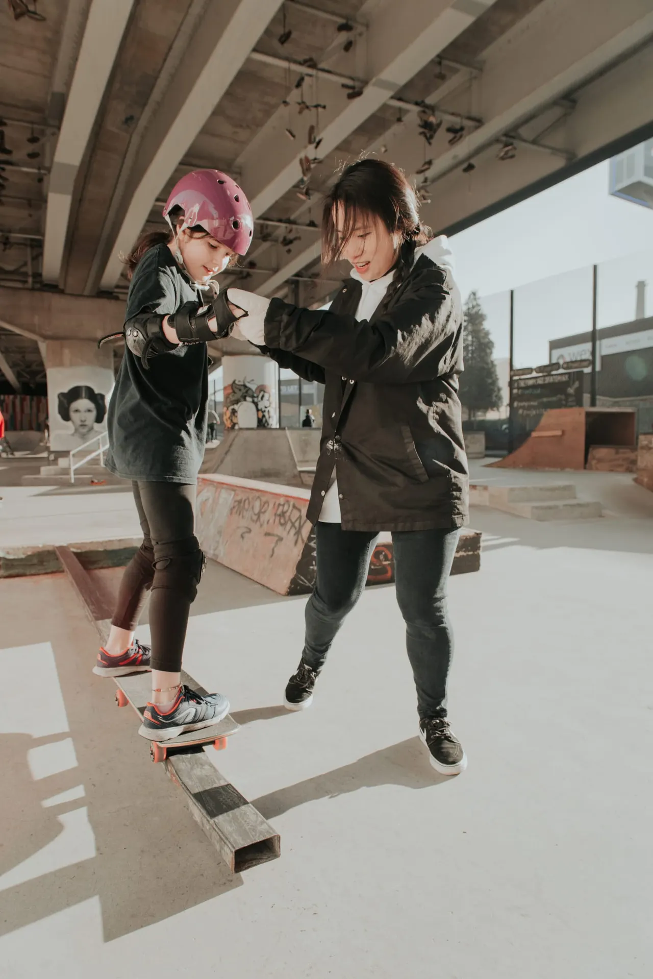 Two young people skateboarding together under a bridge at an indoor skate park.