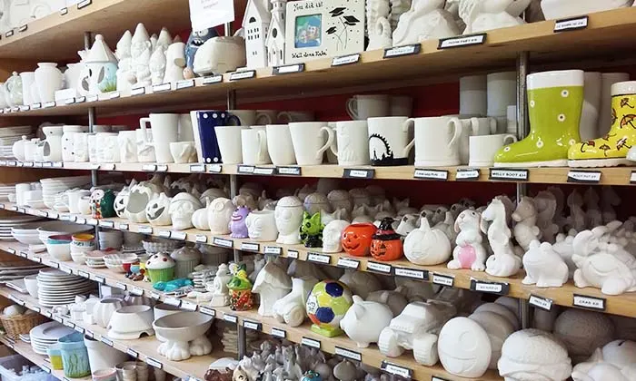 Shop shelves displaying a wide variety of unpainted ceramic pieces including bowls, mugs, figurines and decorative items ready for painting.