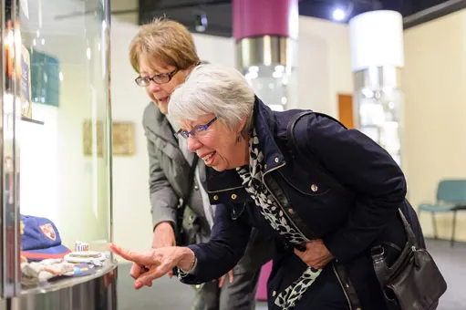 Two older women viewing an exhibit display case together inside a museum gallery space.