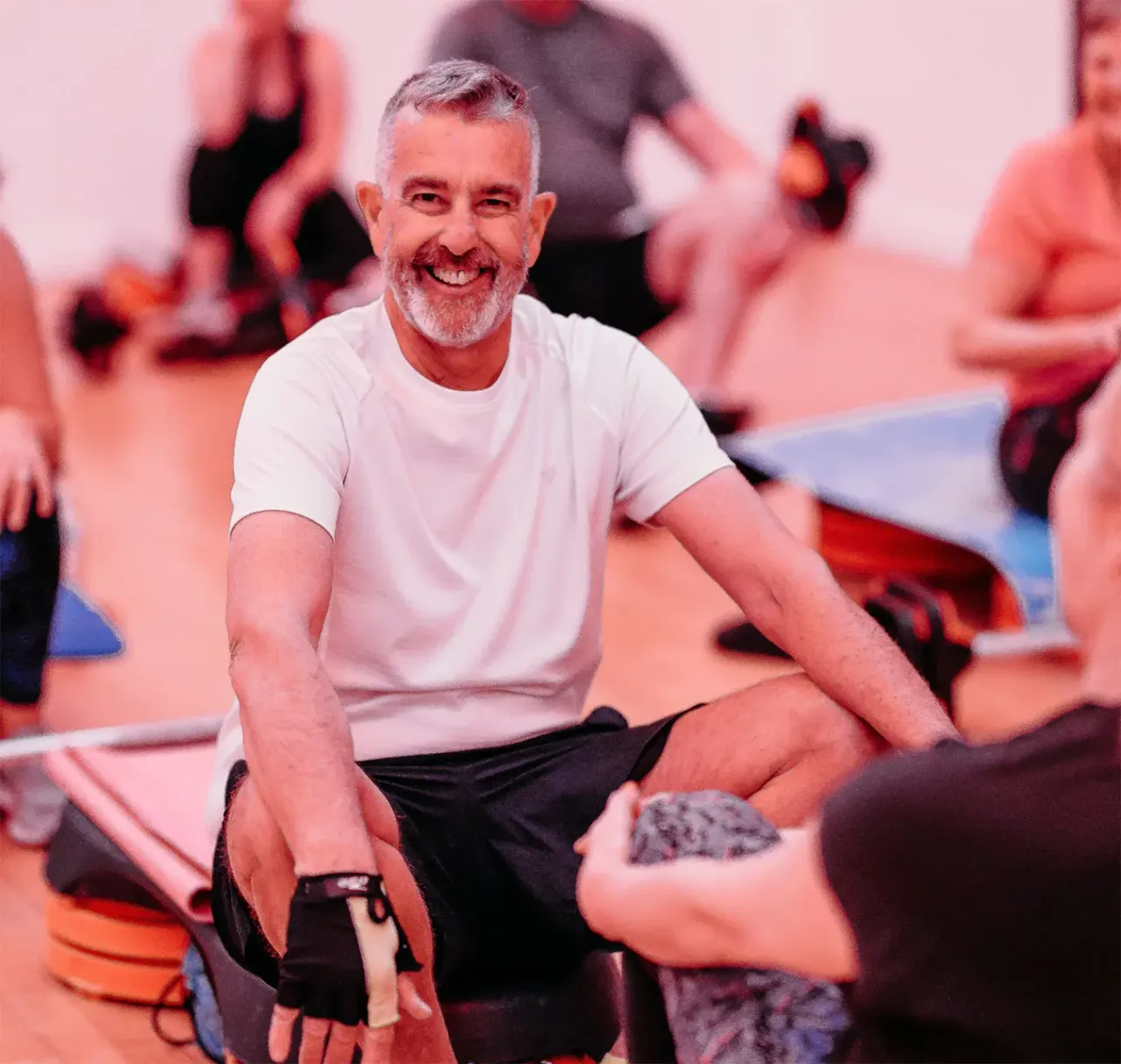Man sitting on floor smiling during a group activity or workshop with other participants in the background.