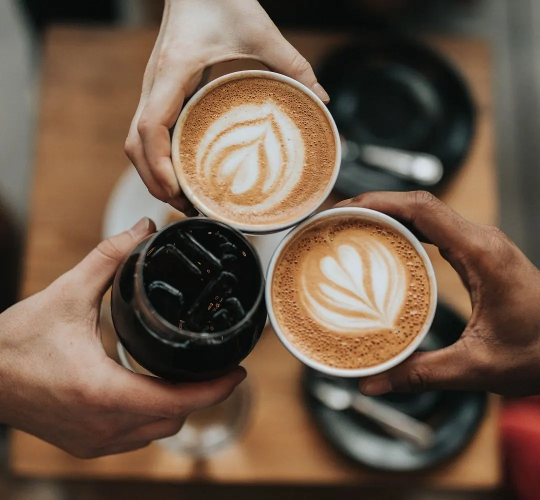 Two people holding three cups of coffee with latte art designs and one black espresso.