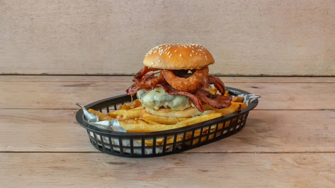 Sesame seed burger with crispy fried chicken, bacon and sauce served in a basket with chips on wooden table.
