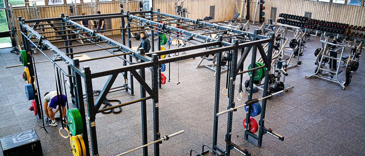 Indoor CrossFit gym with multiple training rigs, weight plates, and exercise equipment arranged across a concrete floor.