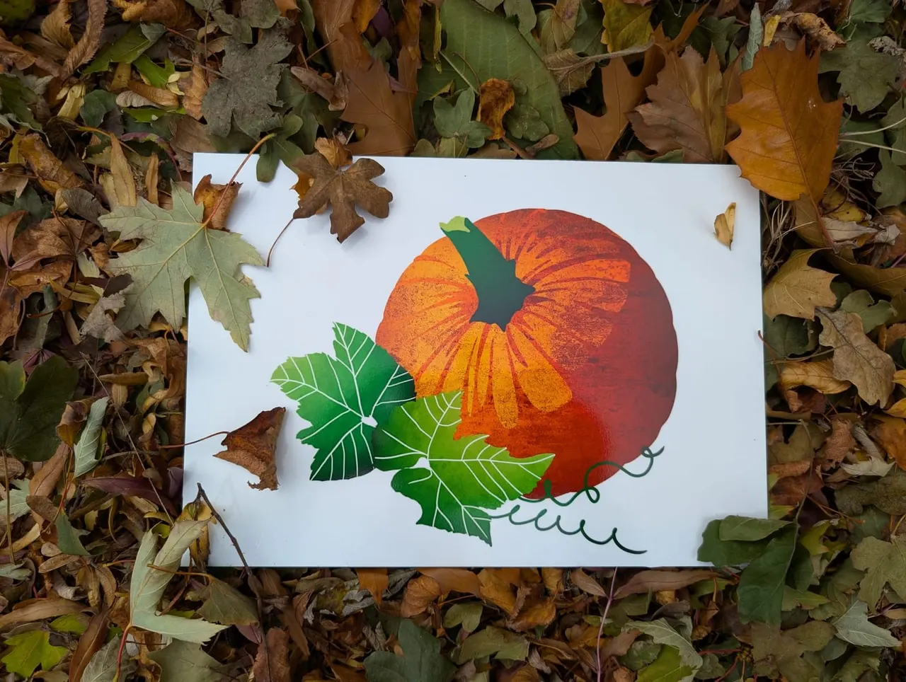 Illustrated autumn greeting card with pumpkin and leaves placed on fallen foliage.