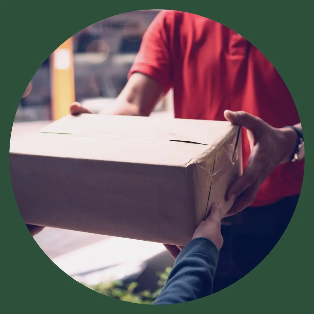 Person in red shirt handing over a cardboard box to another person outdoors.