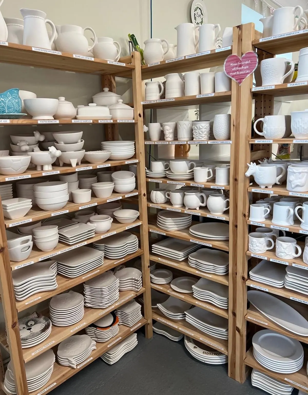 Extensive wooden shelving displaying a collection of white ceramic tableware including plates, bowls, cups, jugs and decorative items.