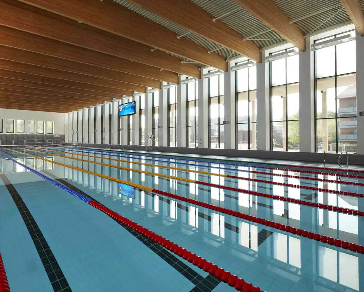 Indoor swimming pool with lane dividers in a modern facility with wooden ceiling and floor-to-ceiling windows.