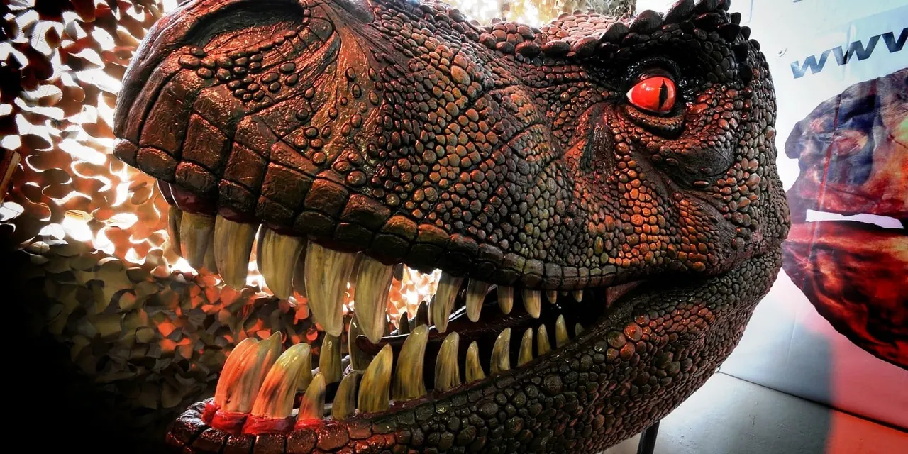 Close-up of a large animatronic dinosaur head with red eye and bared teeth on display.