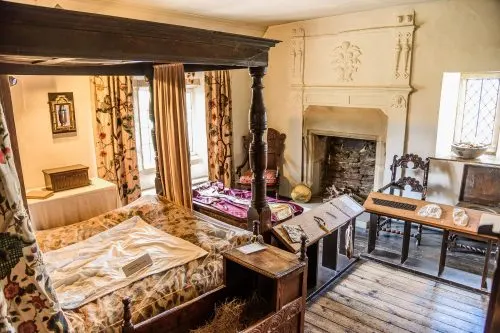 A historic bedroom with a four-poster bed, fireplace, period furniture and traditional decor from the Tudor era.