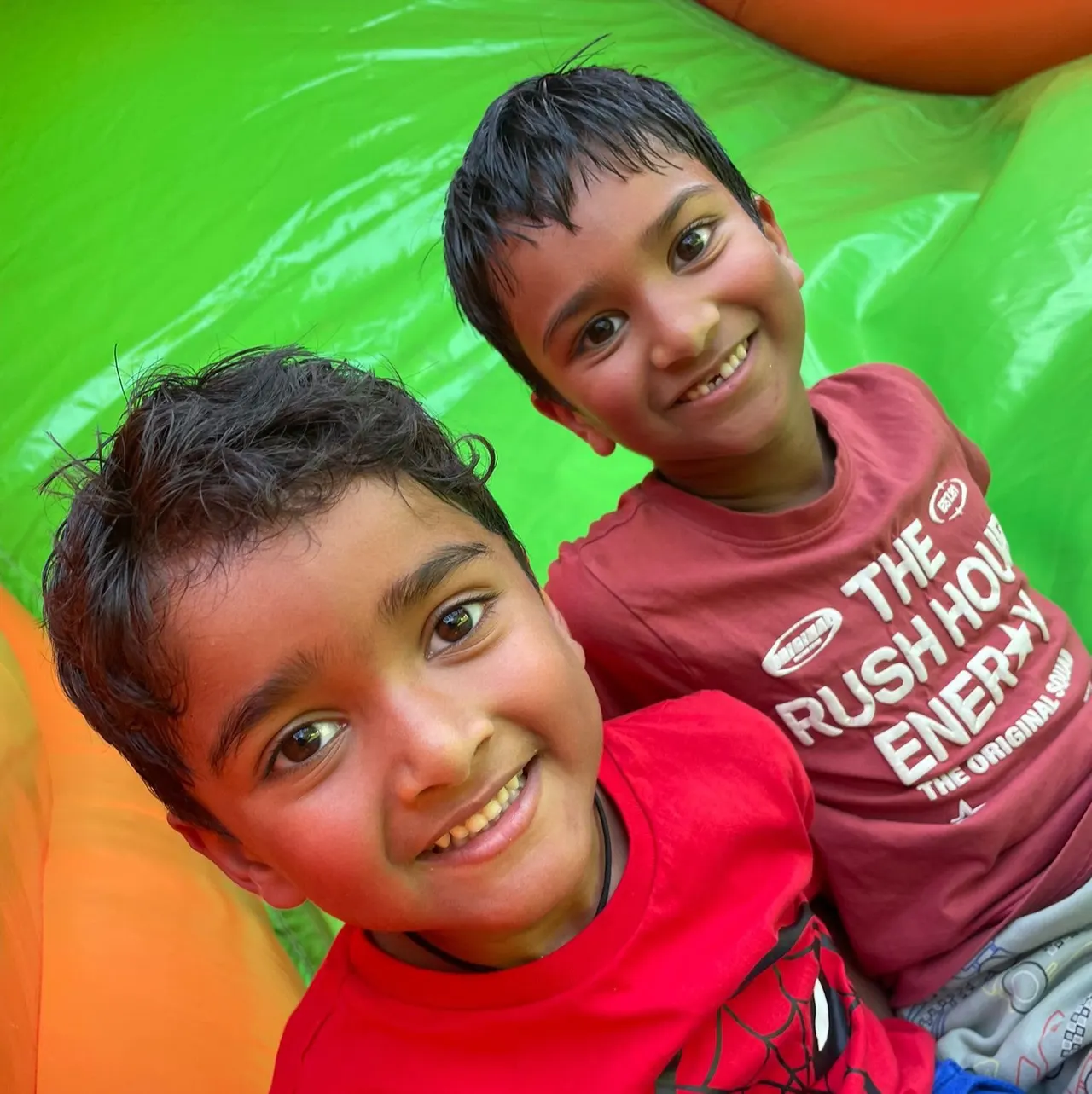 Two young boys smiling at the camera whilst on a bright green inflatable at a leisure venue.