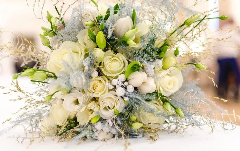 Bridal bouquet of cream roses, white berries and green foliage with grey-green moss accents.