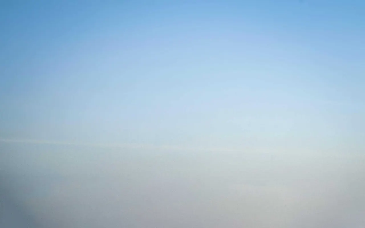 Clear blue sky gradually fading to a hazy horizon over a distant landscape.