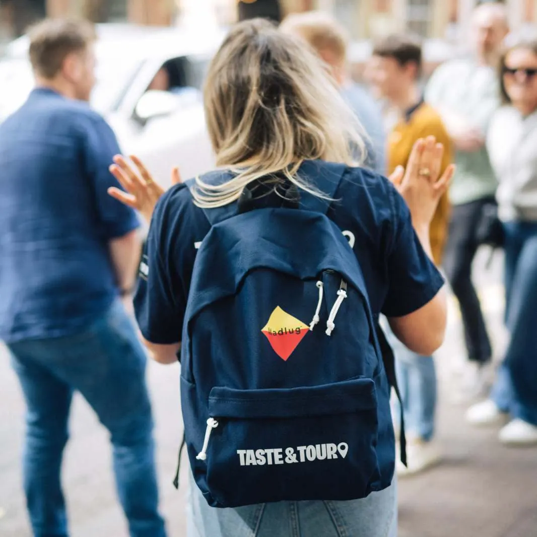 Person wearing a Taste & Tour branded backpack stands in a crowd during an outdoor group tour activity.