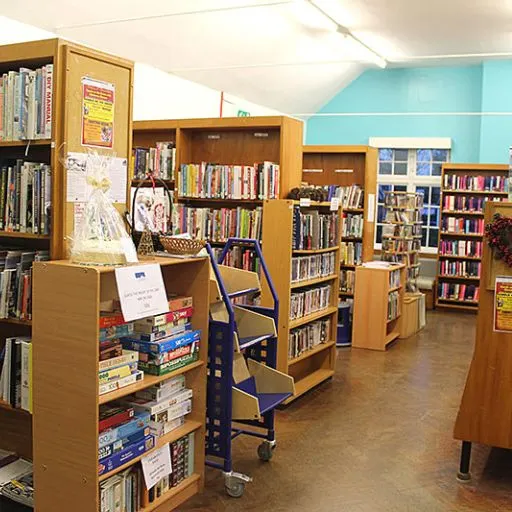 Library interior with wooden shelving units displaying books, with turquoise walls and brown flooring.