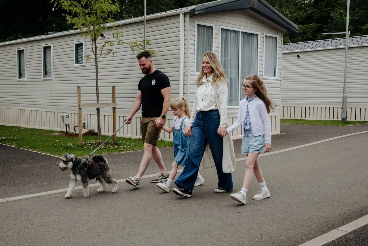 Family of four with a dog walking past static caravans on a holiday park road.