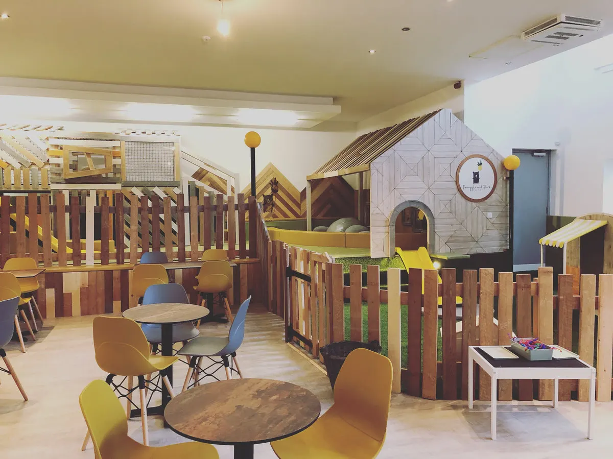 Indoor play area with wooden structures, small tables and chairs, and various play equipment for children.