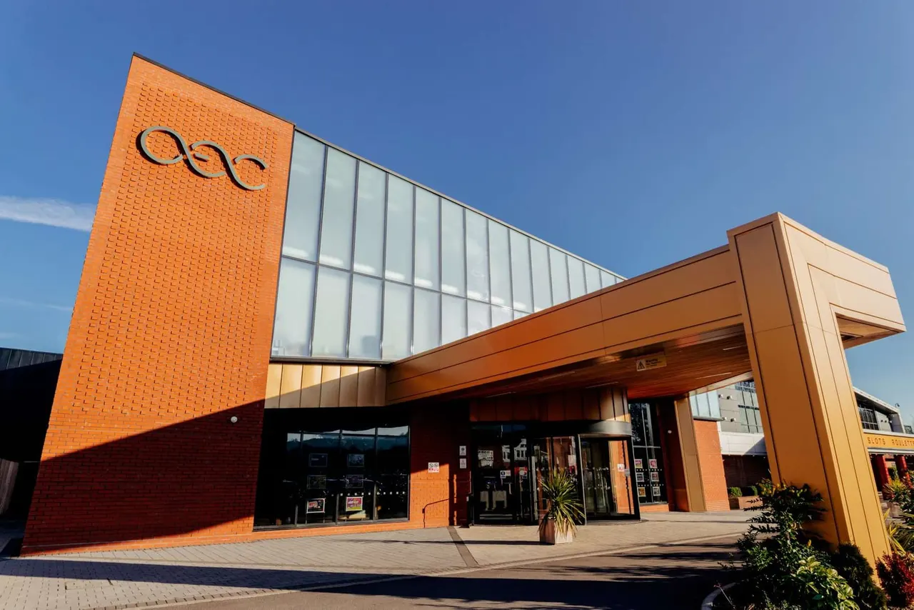 Modern brick building with orange and brown exterior, glass panels, and covered entrance on a clear day.