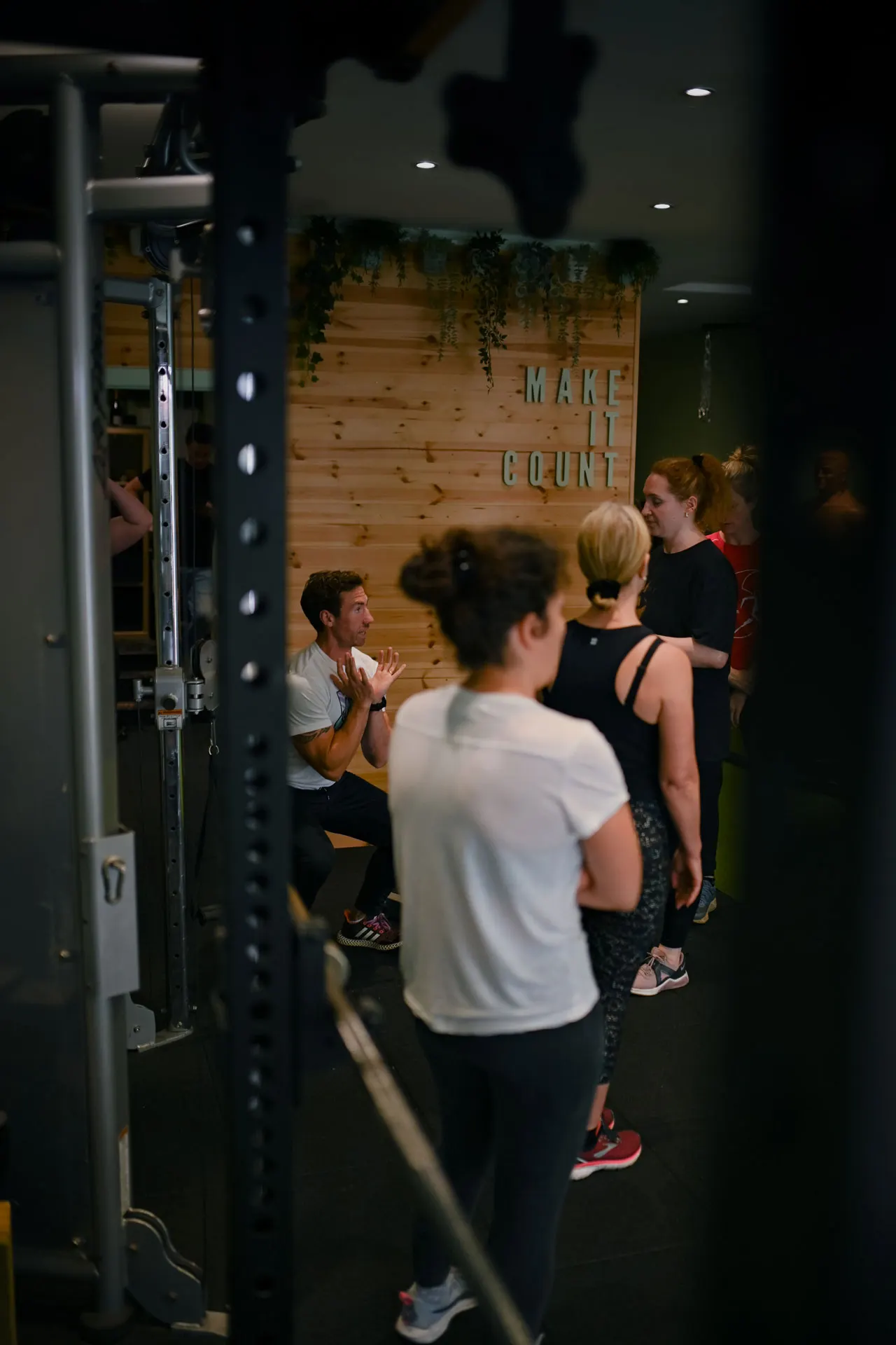 A group of people in athletic wear gather inside a fitness studio with wooden panelling and "MAKE IT COUNT" signage.