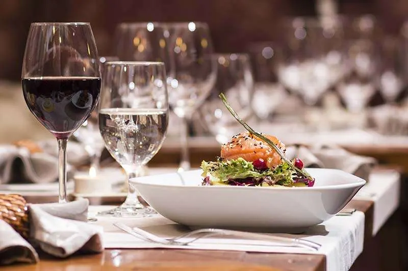 Fine dining table setting with red wine, water glass, and plated salmon dish with salad.