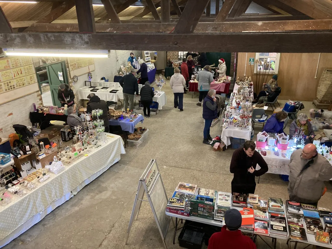 Visitors browse handmade crafts and collectables at market stalls inside an indoor hall with exposed beams.