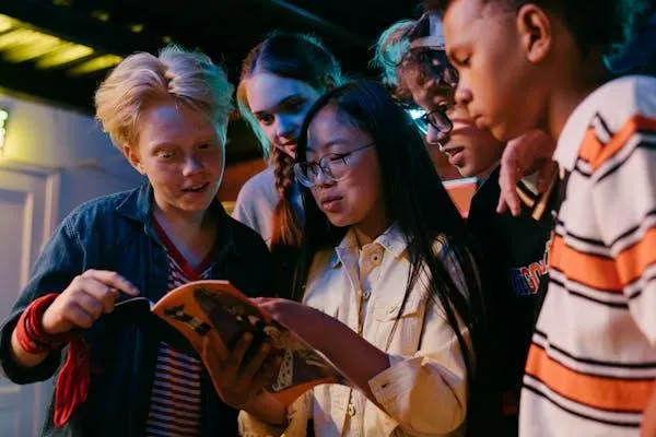 Group of young people gathered indoors under colourful lighting, looking at a map or document together.