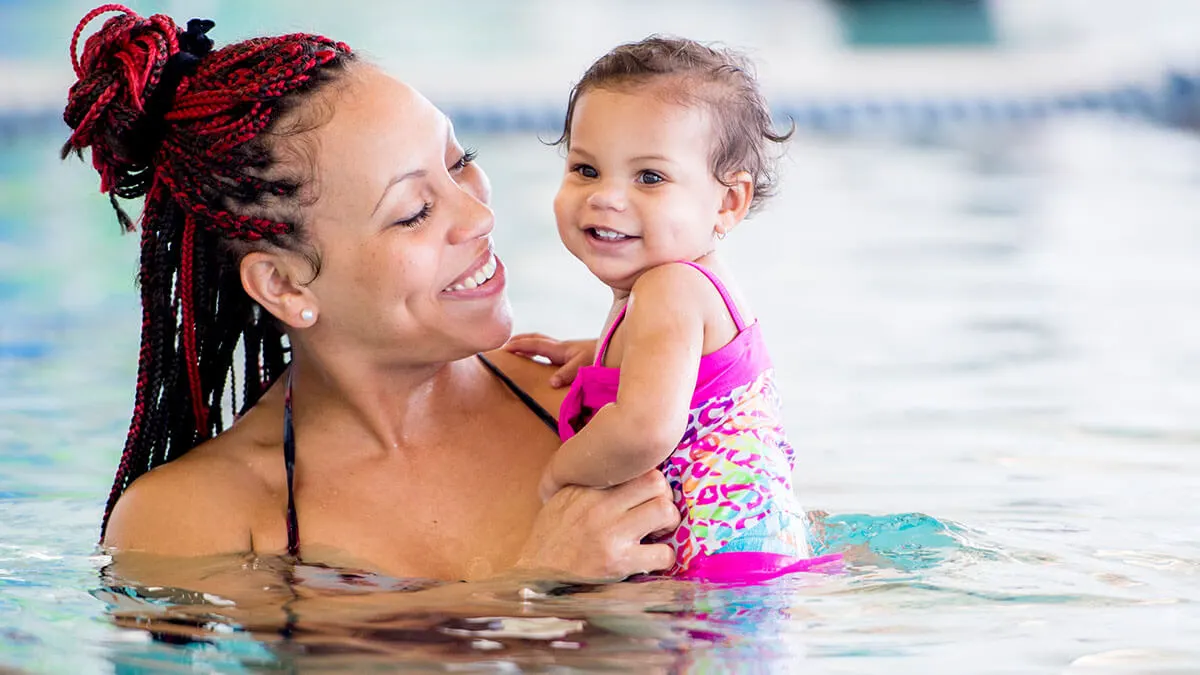 Woman and young child in swimming pool, both smiling.