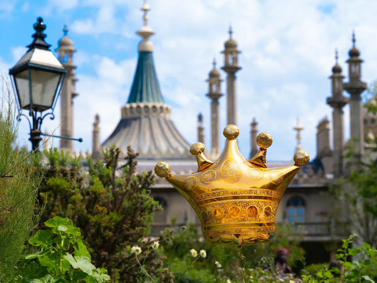 Golden crown decoration in garden with ornate pavilion and minarets in background under blue sky.