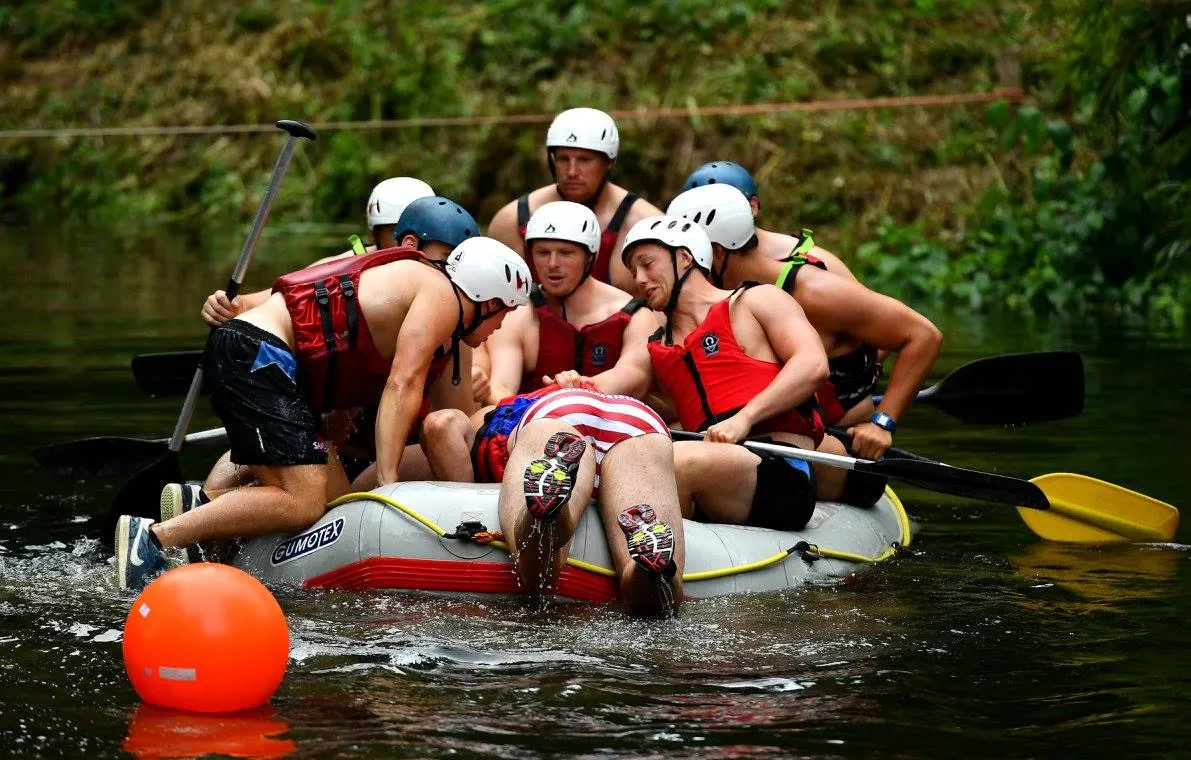 Group of men wearing helmets and life jackets sitting in an inflatable raft on a river.