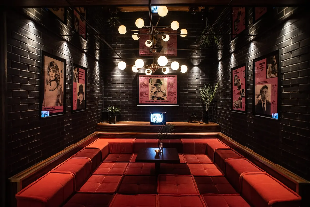 A private screening room with red seating, black brick walls, vintage film posters and a glowing chandelier.