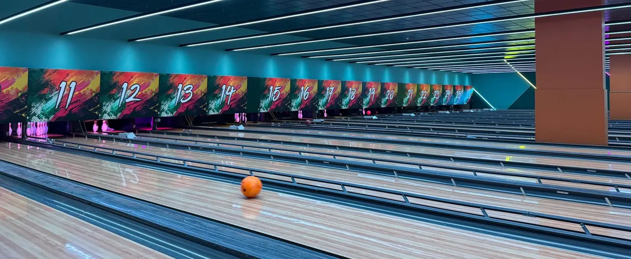 Modern bowling alley interior with multiple lanes, numbered display screens, and an orange bowling ball on the lane.