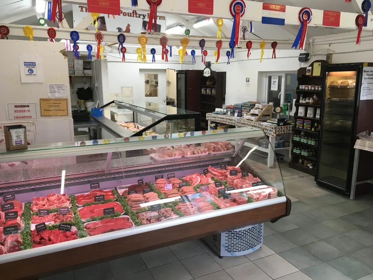 Interior of a poultry farm shop with refrigerated display counters showing various cuts of meat, award ribbons hanging from ceiling.