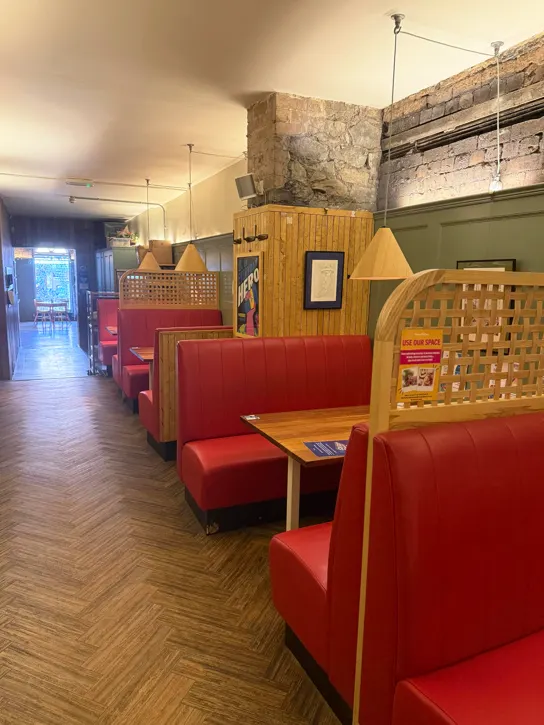 Interior of a café with red booth seating, wooden partitions, pendant lighting, and herringbone flooring.