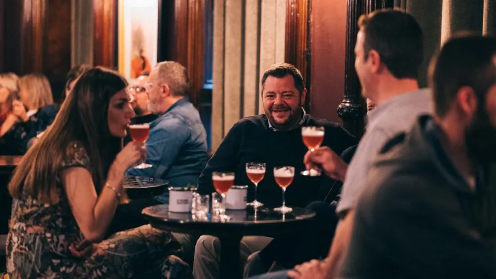 Groups of people socialising at a bar table with cocktails in an evening setting.