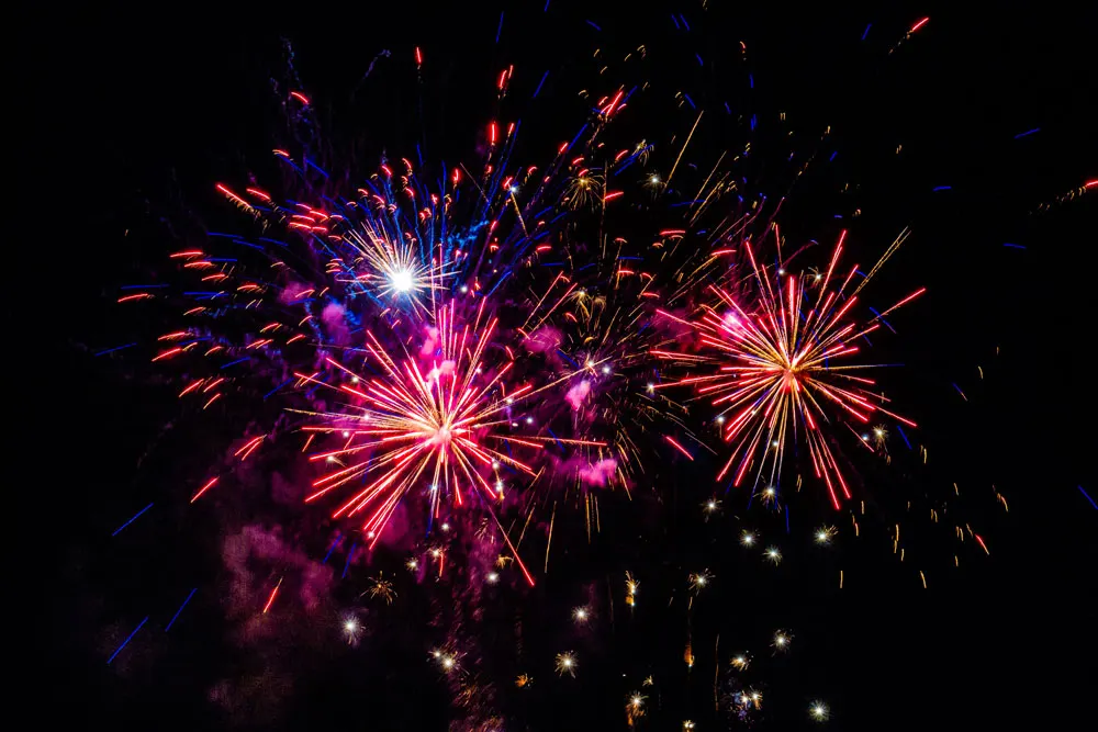 Colourful fireworks bursting in the night sky with red, pink, blue and gold sparks radiating outward.