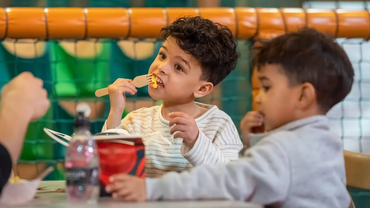 Young children eating snacks at a table inside an indoor play facility.