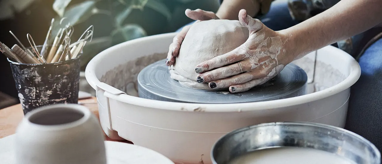 Person shaping clay on a pottery wheel during a ceramic workshop session.