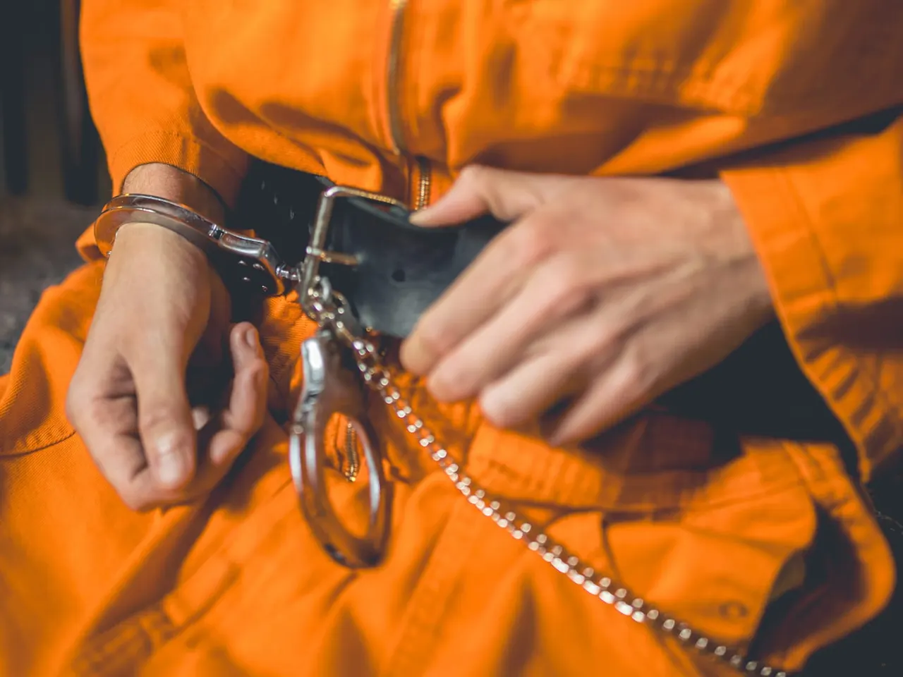 Person in orange clothing holding binoculars and a beaded chain accessory.